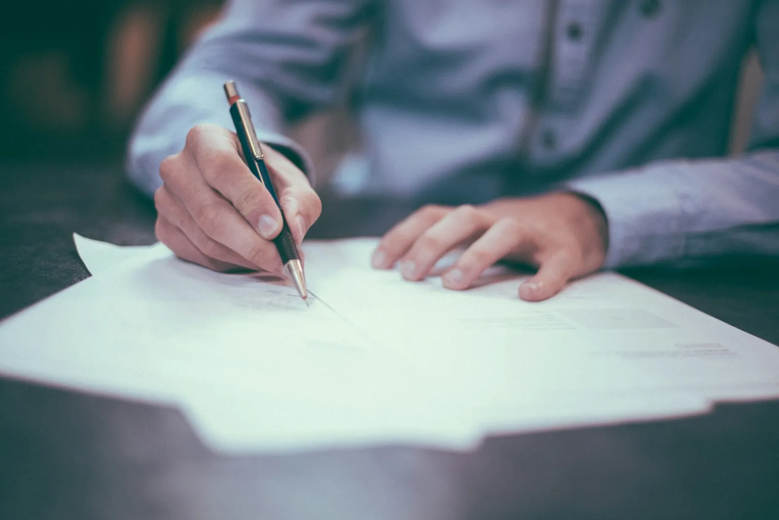 Signing paperwork at a desk with a pen.