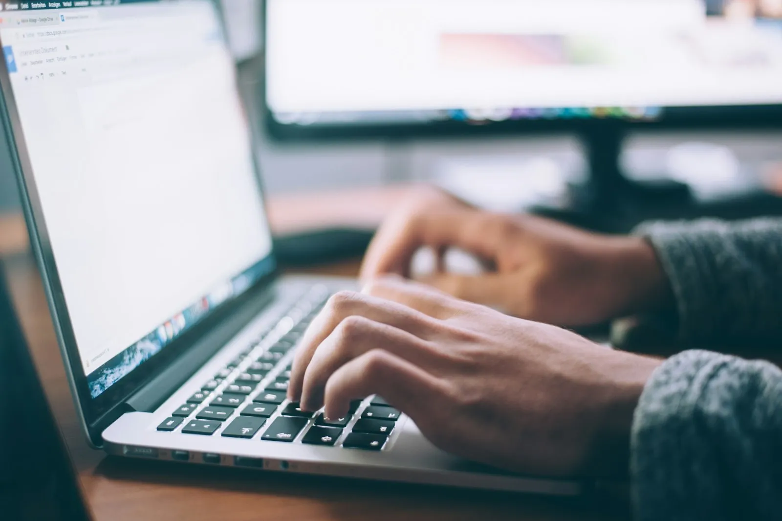 Hands working on a laptop beside a notebook at a meeting table.